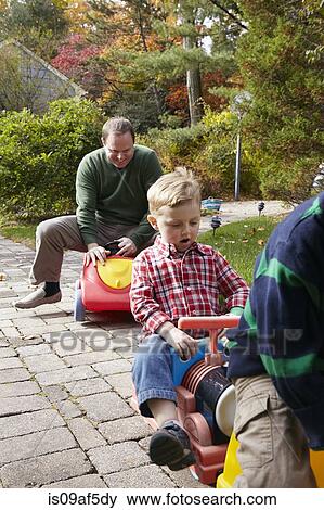 Father and young sons playing on toy cars in garden View Large Photo Image Stock Photo - Father and young sons playing on toy cars in garden. Fotosearch