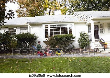 Stock Photography - Father and young sons riding on toy cars in garden. Fotosearch