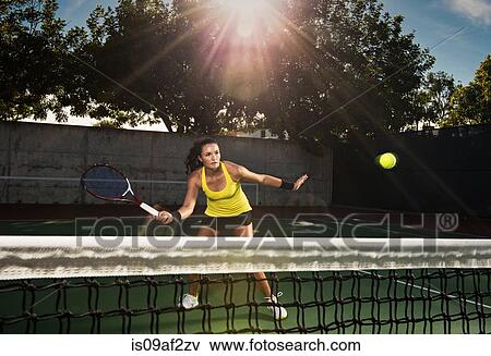Stock Photo - Female tennis player hitting ball over net. Fotosearch