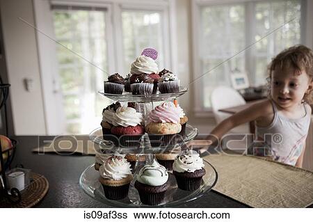 Stock Photograph - Female toddler looking at cake stand full of cupcakes. Fotosearch