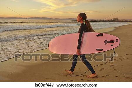 Stock Photo - Girl at beach carrying pink surfboard. Fotosearch