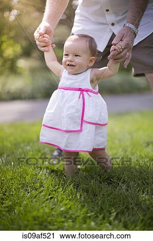 Stock Image - Grandfather helping granddaughter to walk. Fotosearch