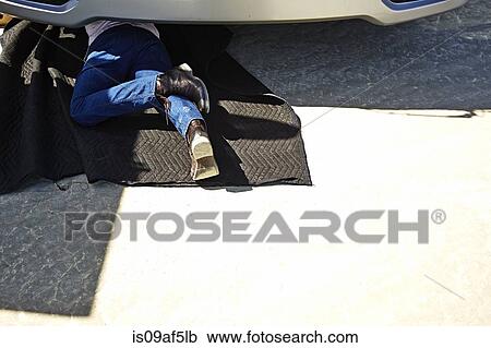 Man lying under a car on mat View Large Photo Image Stock Image - Man lying under a car on mat. Fotosearch