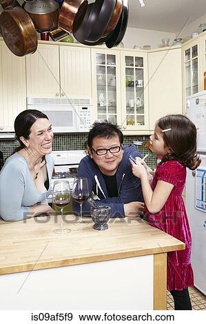 Stock Photo - Mature couple and young daughter in kitchen. Fotosearch