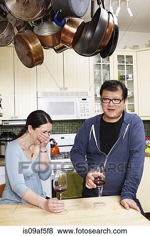 Stock Photo - Mature couple relaxing with a glass of wine in kitchen. Fotosearch