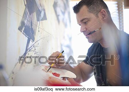 Stock Photography - Mature male artist painting canvas in studio. Fotosearch