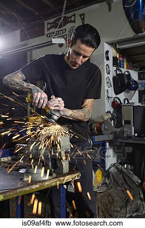 Stock Image - Mature man welding parts in motorcycle repair workshop. Fotosearch