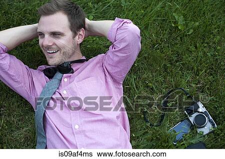 Stock Photograph - Mid adult man with camera and smartphone relaxing on grass. Fotosearch