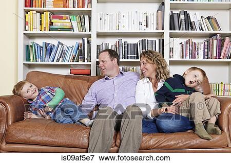 Stock Photo - Mid adult parents and young sons having fun on sofa. Fotosearch