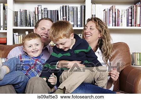 Stock Image - Mid adult parents and young sons sitting on sofa. Fotosearch