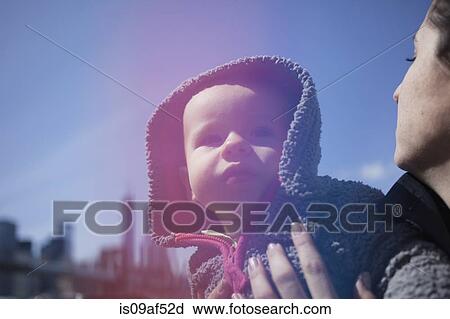 Stock Image - Mother holding daughter wearing hood. Fotosearch