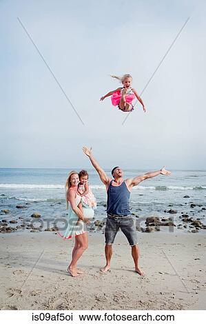 Stock Image - Parents and two young girls fooling around on beach. Fotosearch
