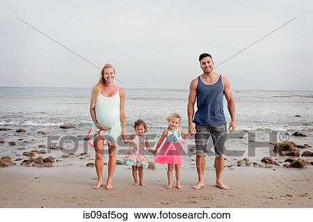 Stock Image - Parents and two young girls strolling on beach. Fotosearch