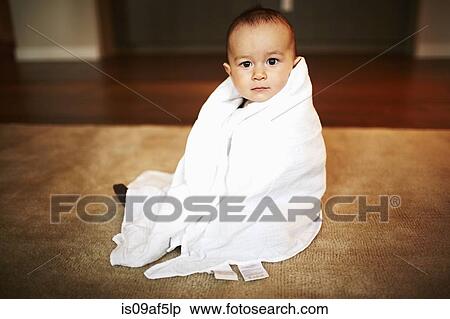 Stock Photography - Portrait of baby boy wrapped in blanket sitting on floor. Fotosearch
