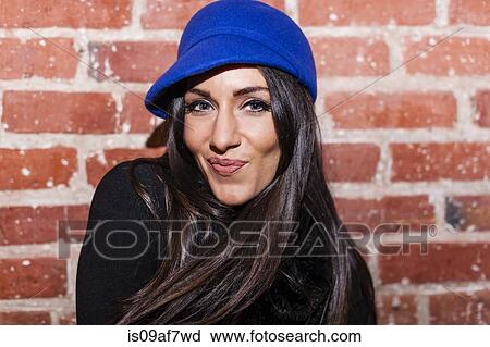 Stock Image - Portrait of mid adult woman in front of brick wall. Fotosearch