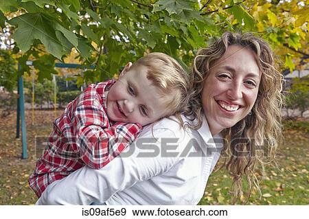 Stock Photo - Portrait of mother giving young son piggy back in garden. Fotosearch