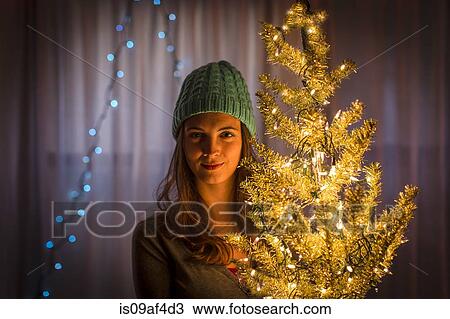 Stock Image - Portrait of young woman holding christmas tree. Fotosearch