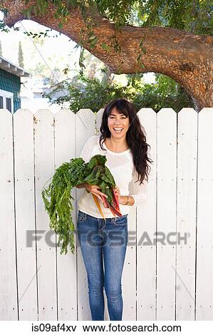 Stock Photo - Portrait of young woman holding homegrown vegetables. Fotosearch