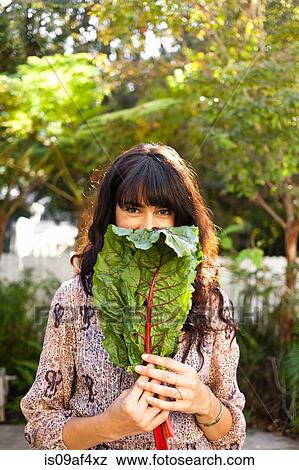 Stock Photo - Portrait of young woman holding vegetable leaf. Fotosearch