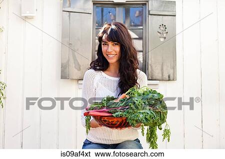 Stock Photograph - Portrait of young woman holding homegrown vegetables. Fotosearch