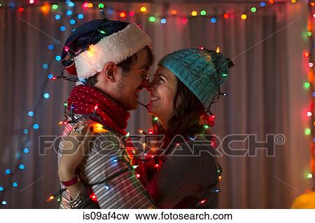 Stock Photo - Romantic young couple wrapped in decorative lights at christmas. Fotosearch