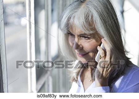 Stock Photo - Senior woman using smartphone whilst looking out of window. Fotosearch