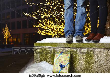 Stock Image - The legs of young couple standing on top of snow covered wall in city. Fotosearch