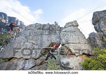 Stock Photograph - Three rock climbers climbing up rock formation. Fotosearch