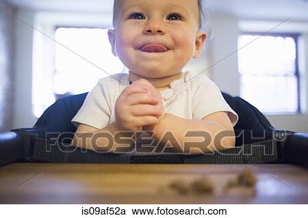Stock Image - Toddler girl licking lips in highchair. Fotosearch