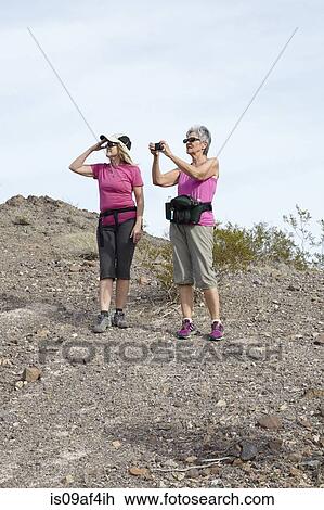 Stock Image - Two senior female hikers looking and photographing view. Fotosearch