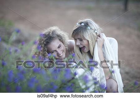 Stock Photography - Two teenage girls looking at wildflowers in woodland. Fotosearch