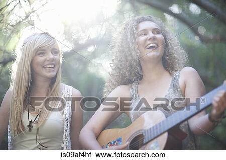Stock Image - Two teenage girls playing guitar in woodland. Fotosearch