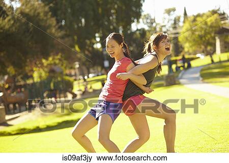Two young women arm in arm and back to back in park View Large Photo Image Stock Photo - Two young women arm in arm and back to back in park. Fotosearch