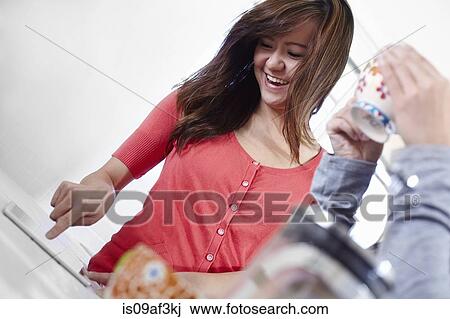 Stock Image - Two young women in kitchen enjoying coffee break. Fotosearch