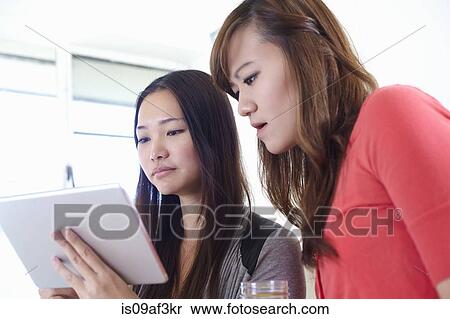 Two young women in kitchen reading digital tablet View Large Photo Image Stock Photography - Two young women in kitchen reading digital tablet. Fotosearch