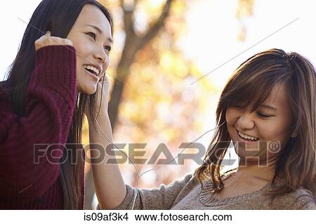 Two young women in park listening to earphones View Large Photo Image Picture - Two young women in park listening to earphones. Fotosearch