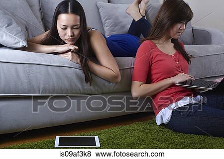 Stock Photo - Two young women in sitting room with digital tablets. Fotosearch