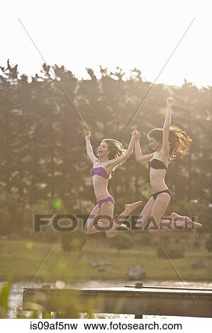Two young women jumping off river pier View Large Photo Image Stock Photo - Two young women jumping off river pier. Fotosearch