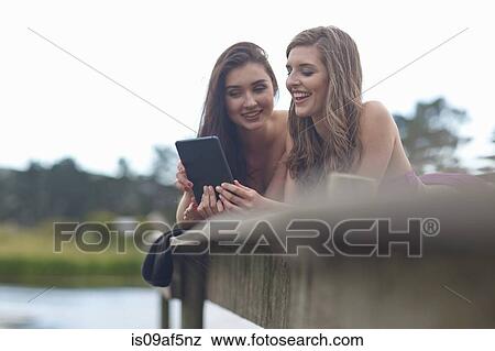 Two young women on river pier looking at digital tablet View Large Photo Image Stock Photo - Two young women on river pier looking at digital tablet. Fotosearch