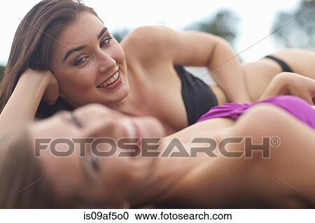 Stock Image - Two young women on river pier sunbathing. Fotosearch