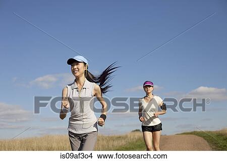 Picture - Two young women running along dirt track. Fotosearch