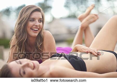 Stock Image - Two young women sunbathing on river pier. Fotosearch