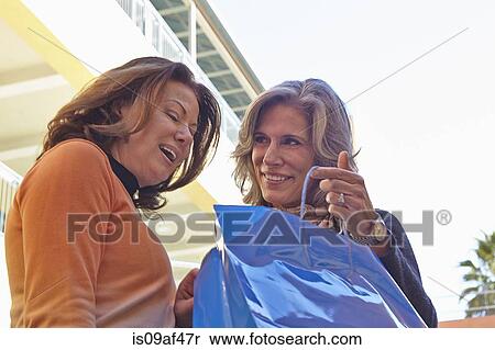 Stock Photography - Woman looking into friend's shopping bag. Fotosearch