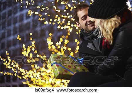 Picture - Young couple exchanging gifts next to outdoor xmas lights. Fotosearch