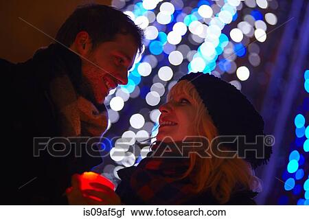 Stock Image - Young couple holding candle in front of city xmas lights. Fotosearch