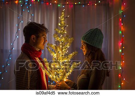 Young couple holding illuminated christmas tree View Large Photo Image Stock Photography - Young couple holding illuminated christmas tree. Fotosearch