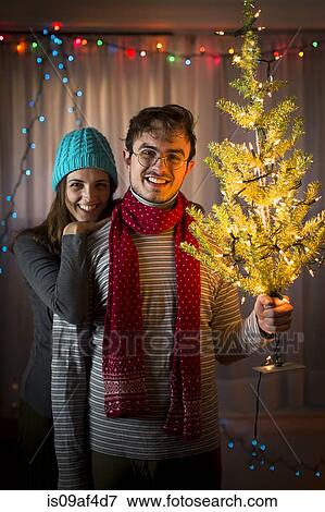 Stock Photo - Young couple holding up illuminated christmas tree. Fotosearch