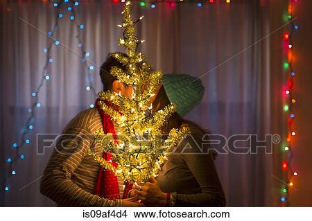 Picture - Young couple kissing behind illuminated christmas tree. Fotosearch
