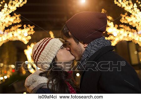 Stock Image - Young couple kissing on street at christmas. Fotosearch