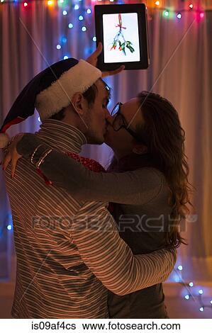 Young couple kissing whilst holding up digital tablet at christmas View Large Photo Image Stock Photograph - Young couple kissing whilst holding up digital tablet at christmas. Fotosearch